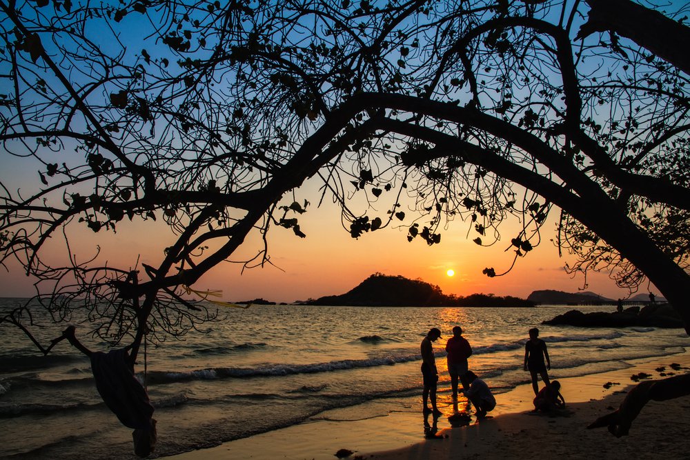 Three people under a tree bough at sunset on a beach in Costa Rica