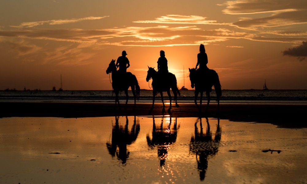 three people on horseback at sunset in Montezuma Beach Costa Rica