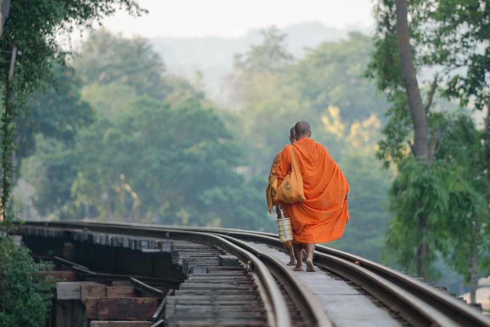 2 monks in orange robes walking on railway