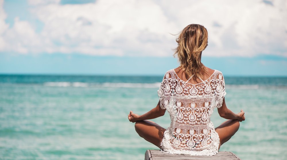 blonde girl in lace top doing yoga facing the beach