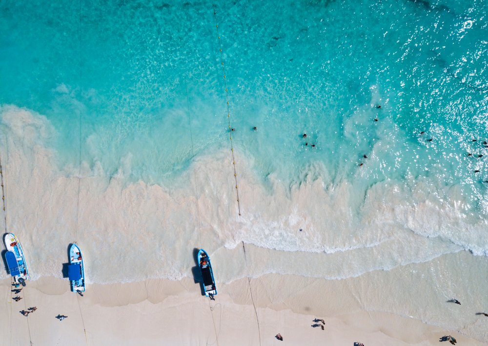 drone view of blue water, creamy sand and 3 boats